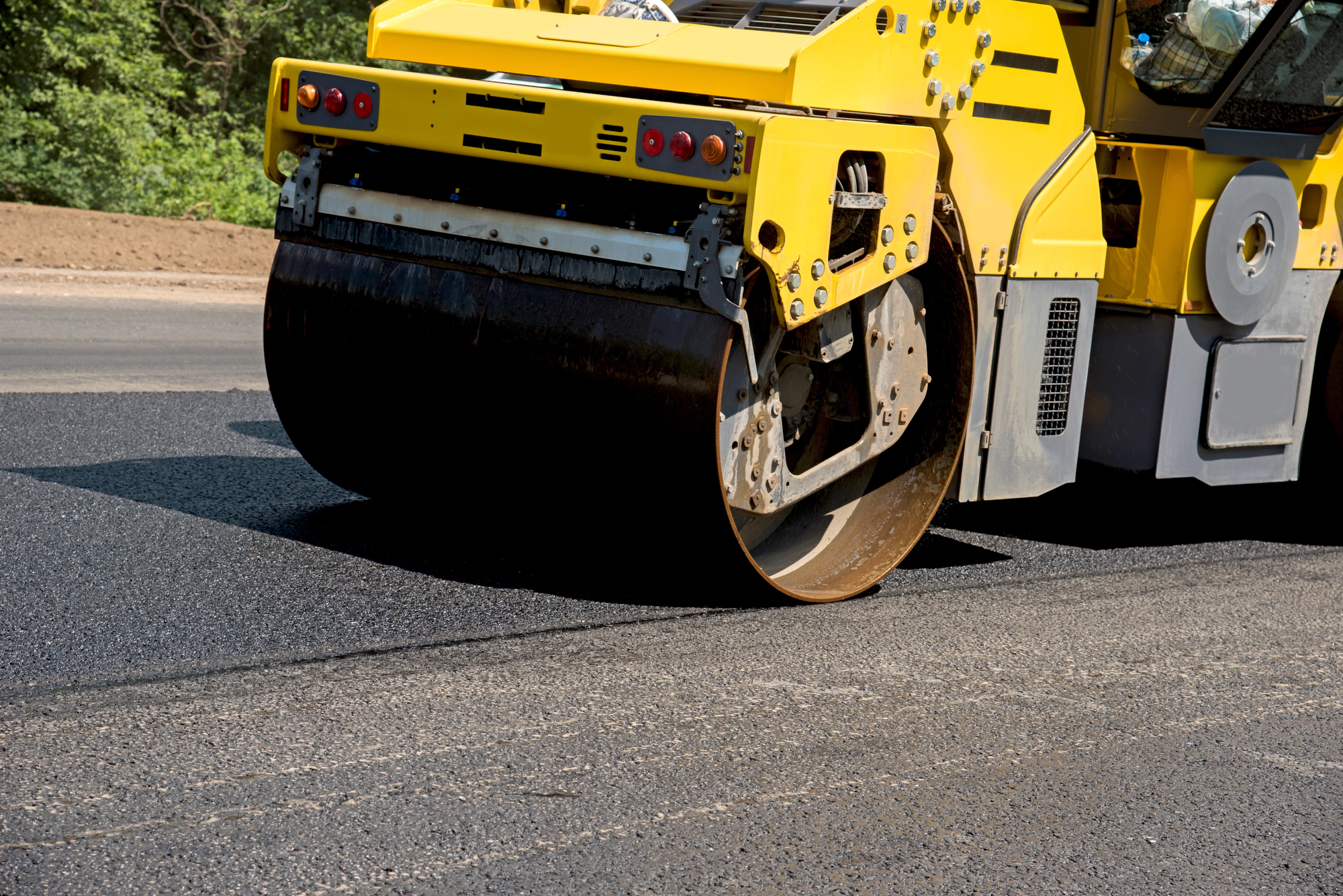 A close-up of a yellow road roller compacting freshly laid asphalt on a road construction site.